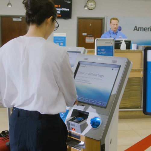 A passenger uses a kiosk to check in as an agent from American Airlines works in the background at Rochester International Airport.