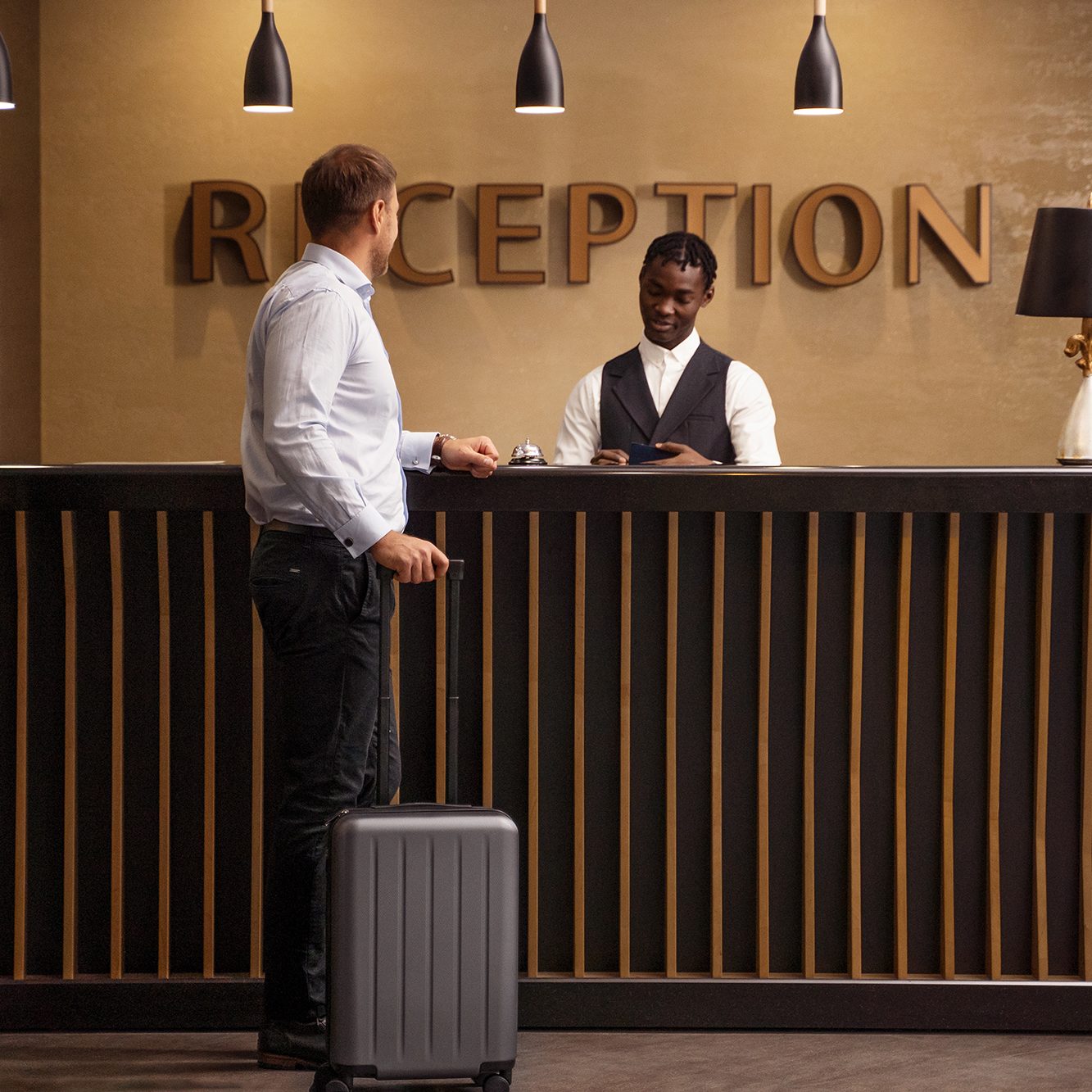 Man with suitcase checking in with man behind hotel reception desk